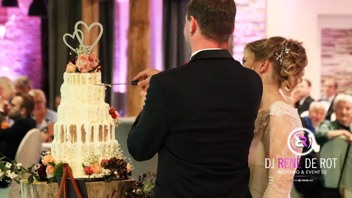 Brautpaar schneidet feierlich die Hochzeitstorte an, DJ sorgt für Musik